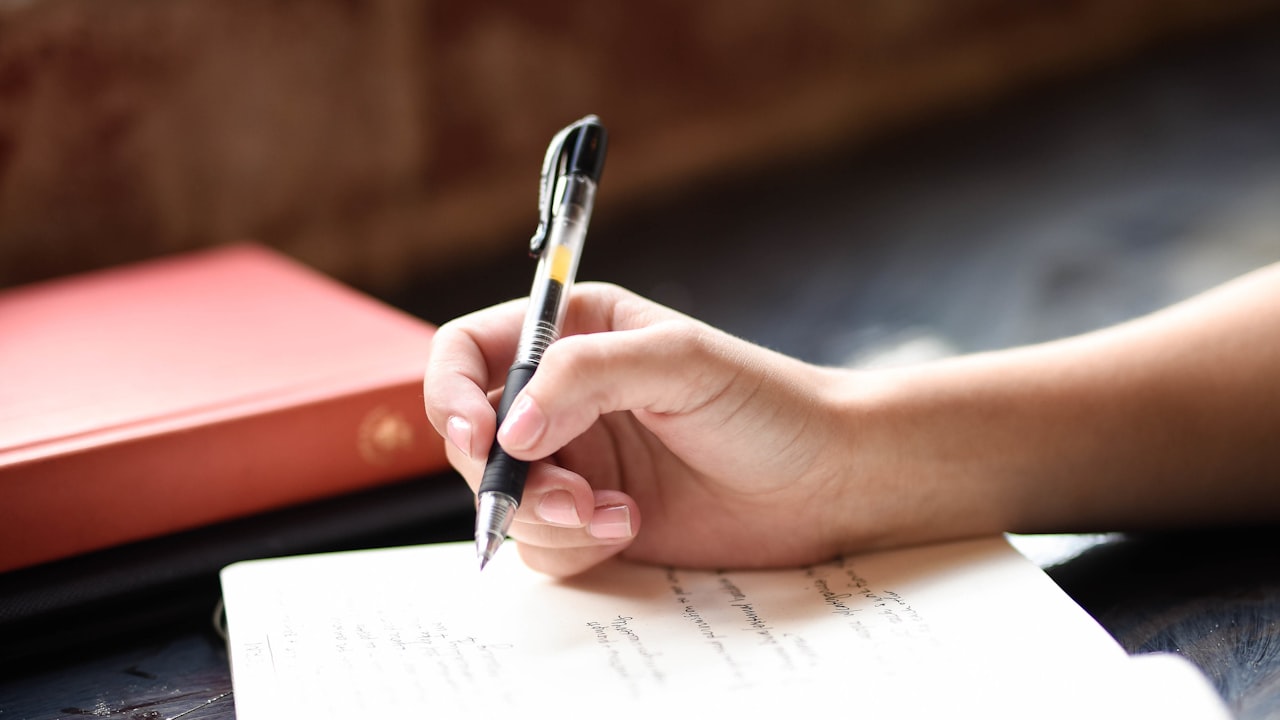Persona escribiendo a mano en un cuaderno junto a una ventana