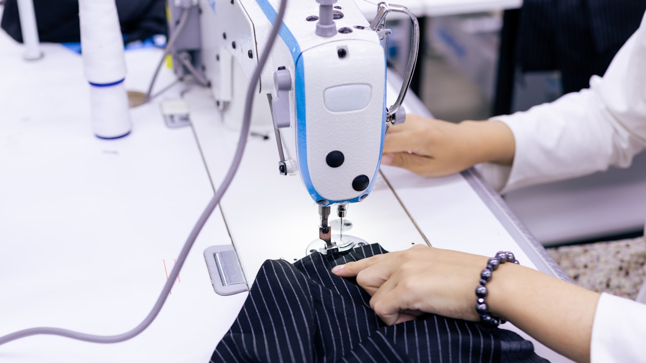 Manos cosiendo a máquina un traje de rayas, hecho a medida